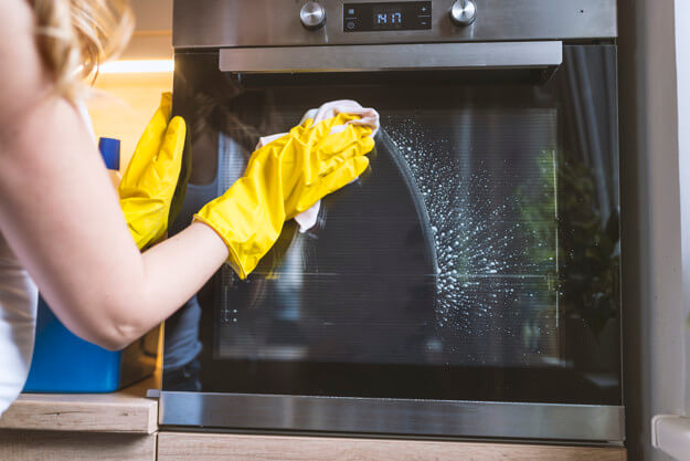 young smiling woman in protective glove with rag cleaning oven.